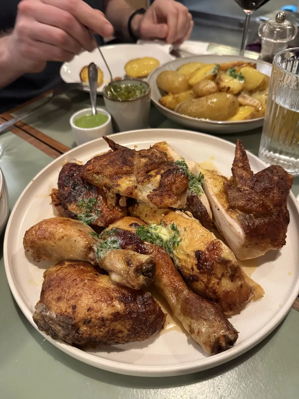 A large plate of roast rotisserie chicken pieces with herbs, potatoes and dips alongside.